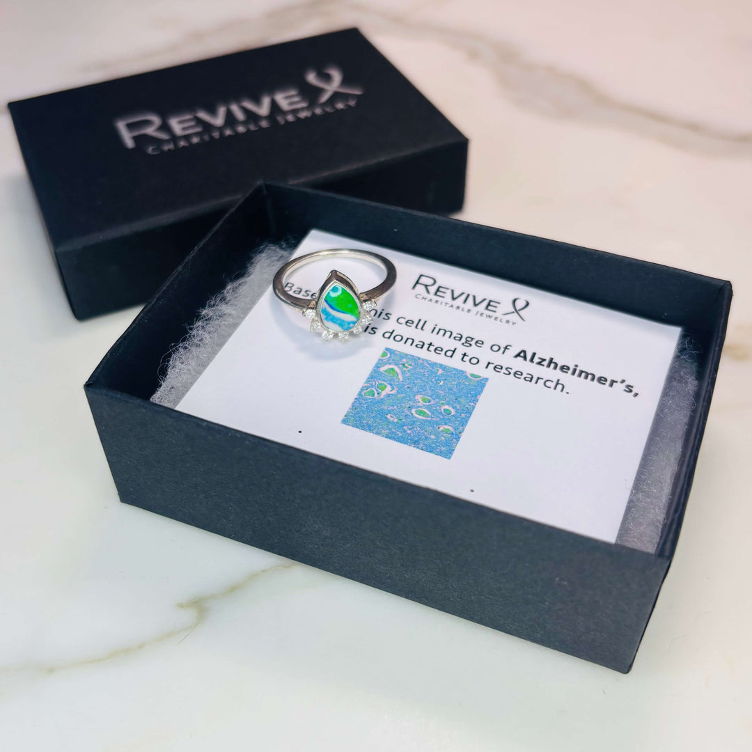 Sterling silver teardrop shaped ring with half halo of cubic zirconia stones and alzheimers cell image under resin pendant with product packaging