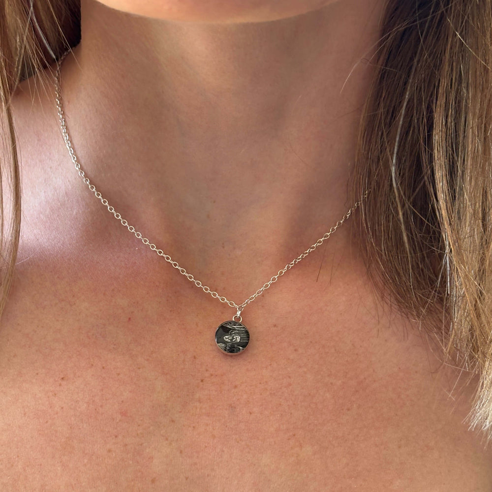 Model wearing silver necklace with a round black and white sonogram pendant 