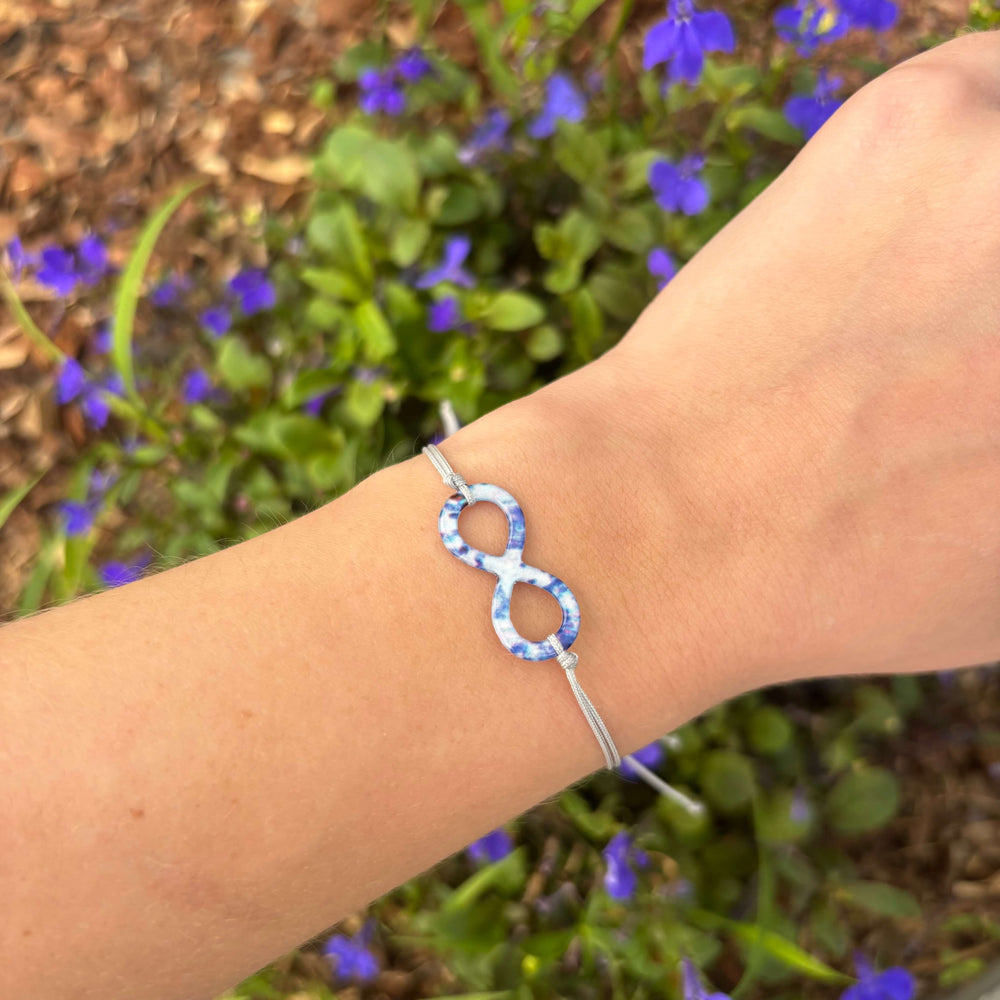model wearing infinity symbol bracelet based on a colon cancer cell image in resin with adjustable gray cord and Sterling silver slide bead