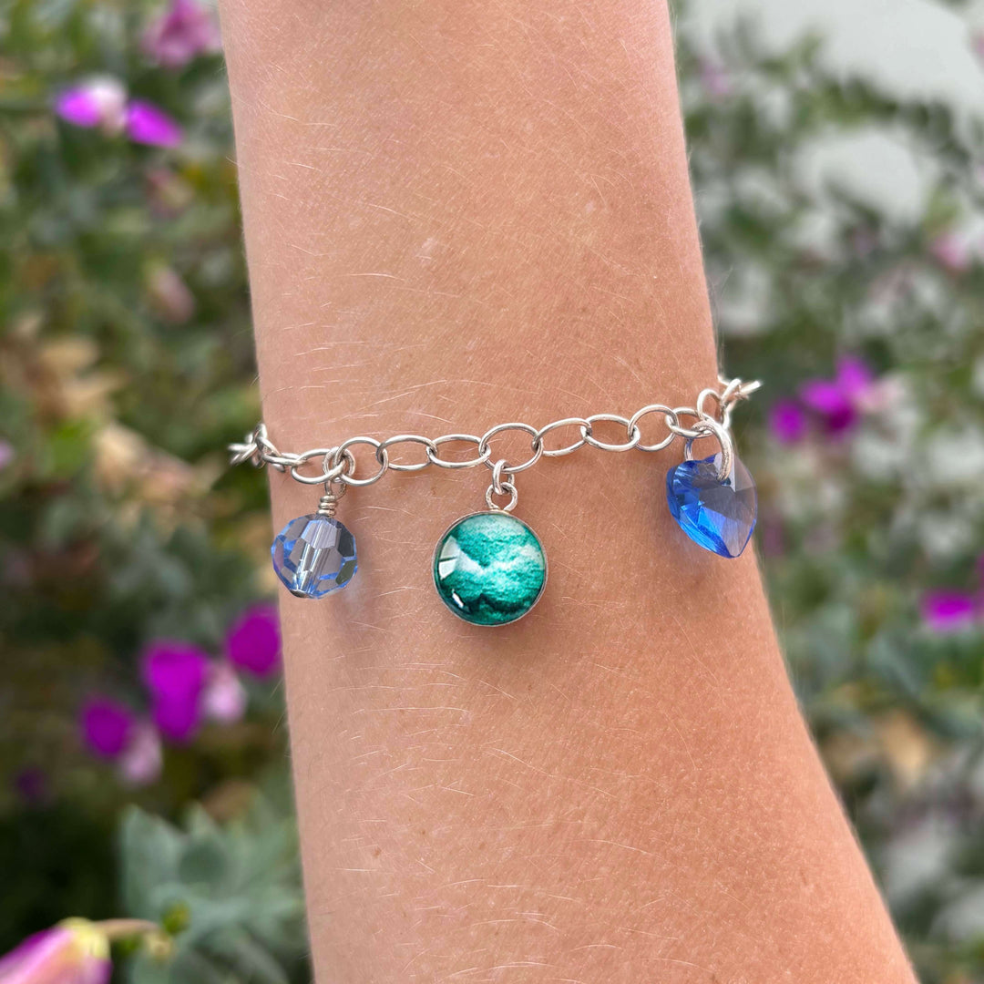 Model wearing Silver bracelet with teal embryo images and blue crystals on a natural background