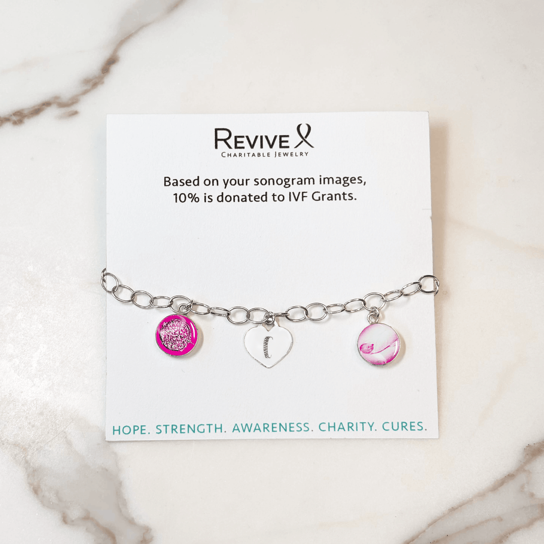 Silver bracelet with pink pendants showing the IVF journey from embryo to baby and an engraved heart-shaped charm on a marble background