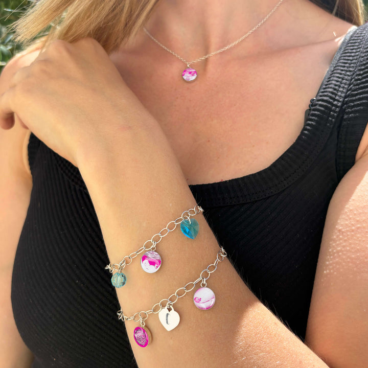 Model wearing silver charm bracelets featuring embryo, sonogram and baby pictures with colorful birthstone crystals and an engraved heart shaped pendant as well as a matching silver necklace.