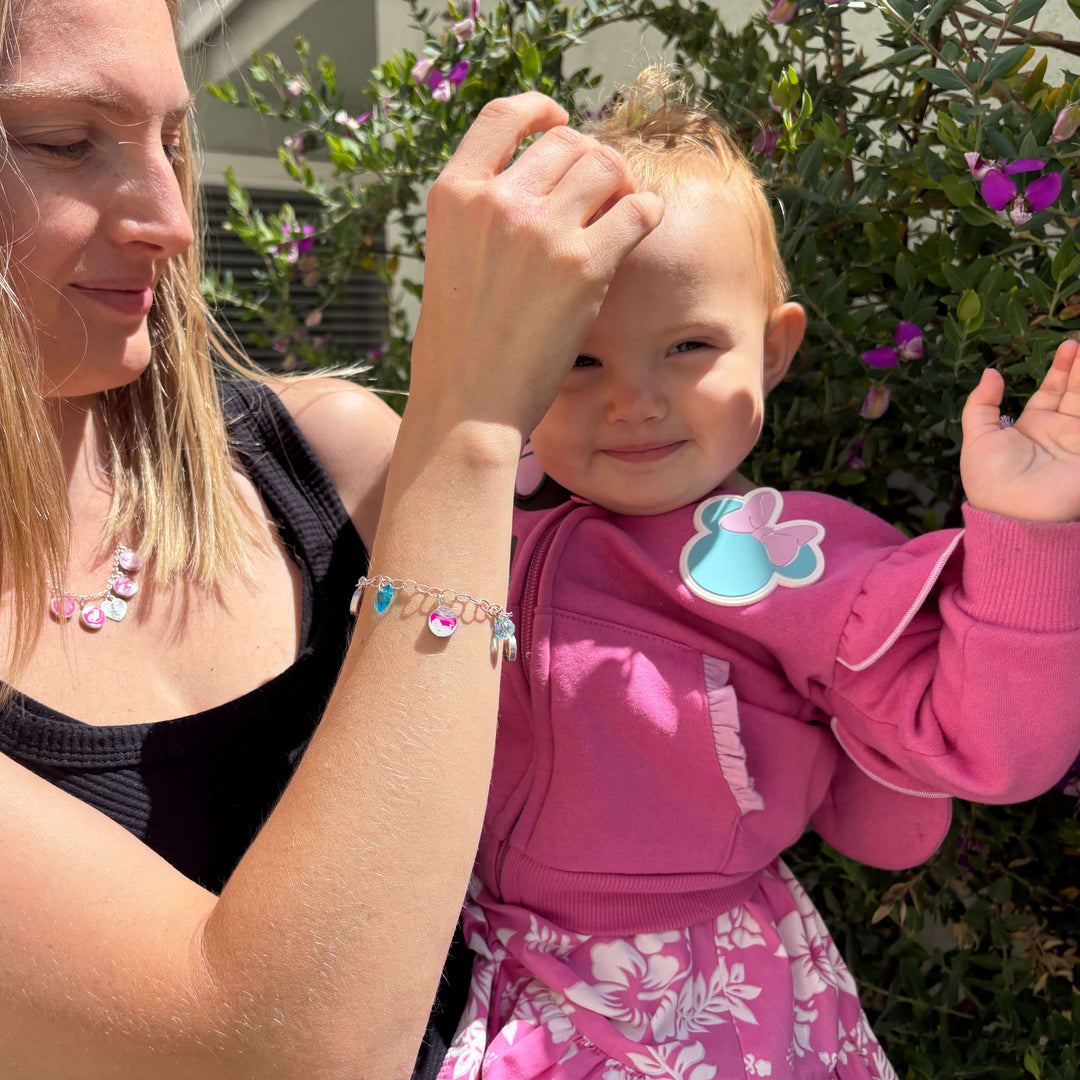 Model holding baby while wearing silver charm bracelet featuring a sonogram image, colorful birthstone crystals and a matching silver necklace.