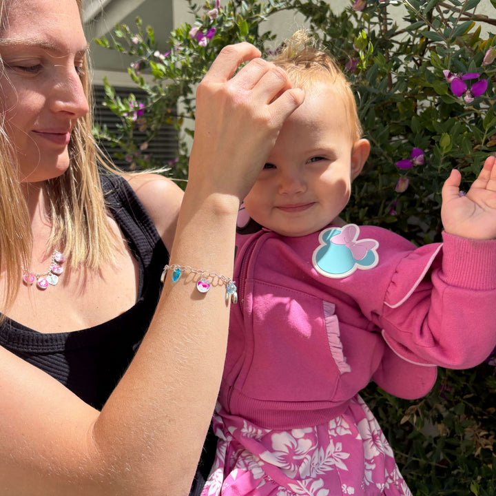 Model holding baby while wearing silver charm bracelet featuring a sonogram image, colorful birthstone crystals and a matching silver necklace.