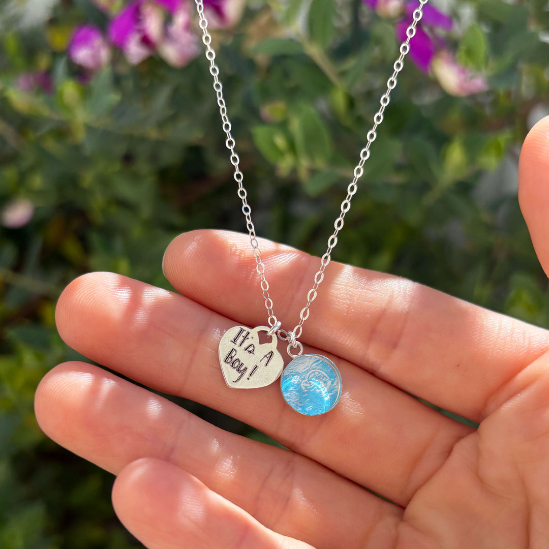 Silver Necklace with Blue Sonogram Image Pendant and "It's A Boy!" Heart-Shaped Engraved Charm held in hand against a natural background.