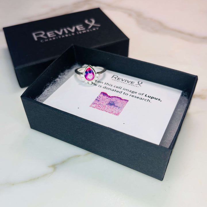 Sterling silver teardrop shaped ring with half halo of cubic zirconia stones and lupus cell image under resin pendant with product packaging