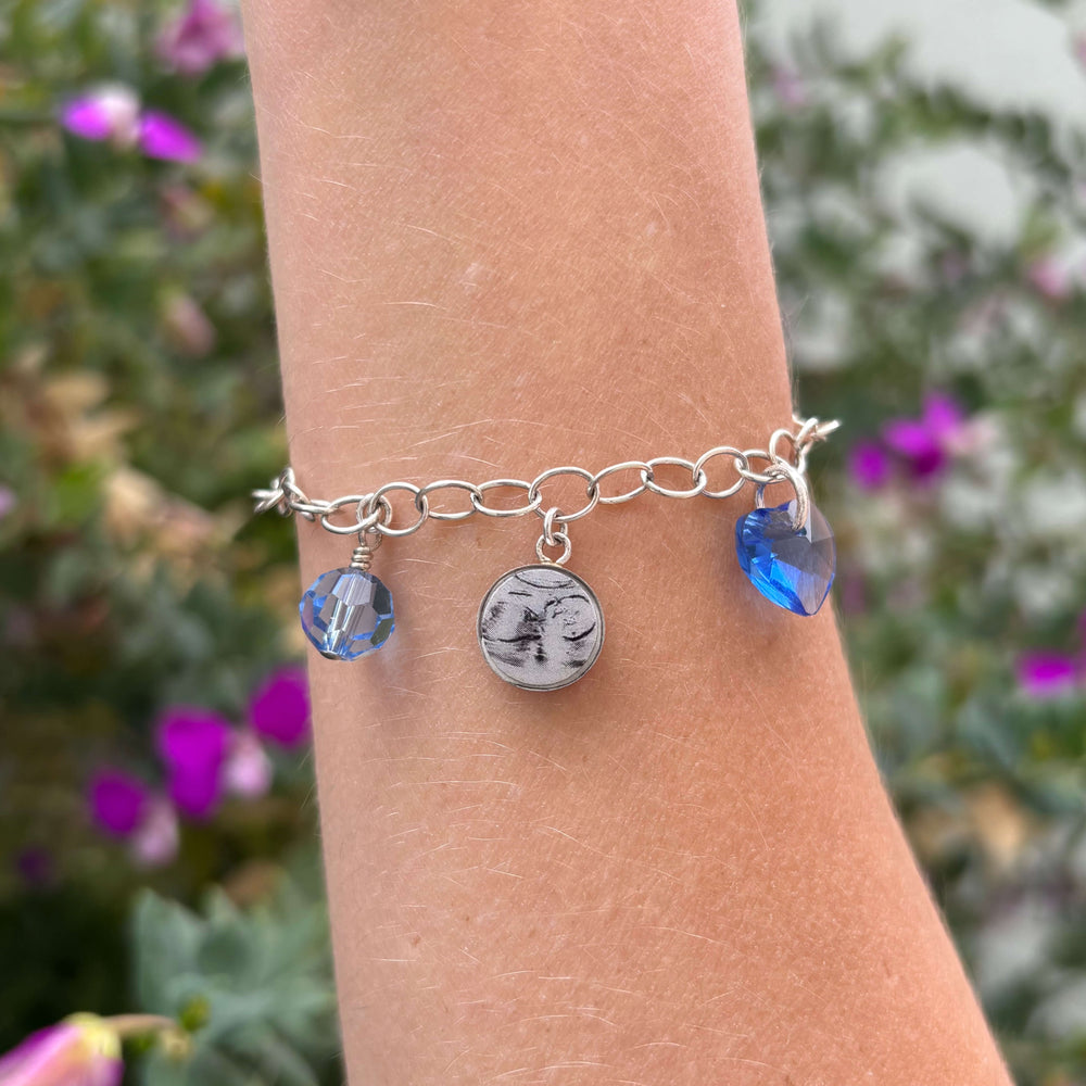 Model wearing silver bracelet with grayscale sonogram pendants with blue birthstone crystals