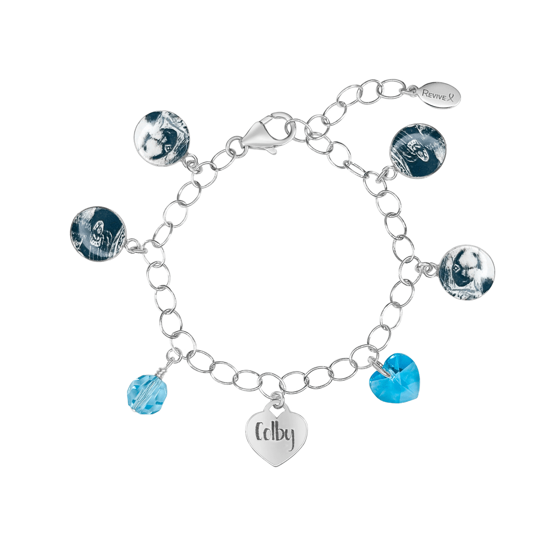 Silver bracelet with grayscale sonogram pendants with blue birthstone crystals and a heart-shaped charm engraved with "Colby"on a white background