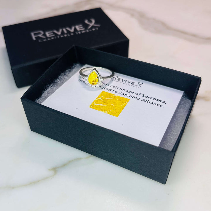 Sterling silver teardrop shaped ring with half halo of cubic zirconia stones and sarcoma cell image under resin pendant with product packaging