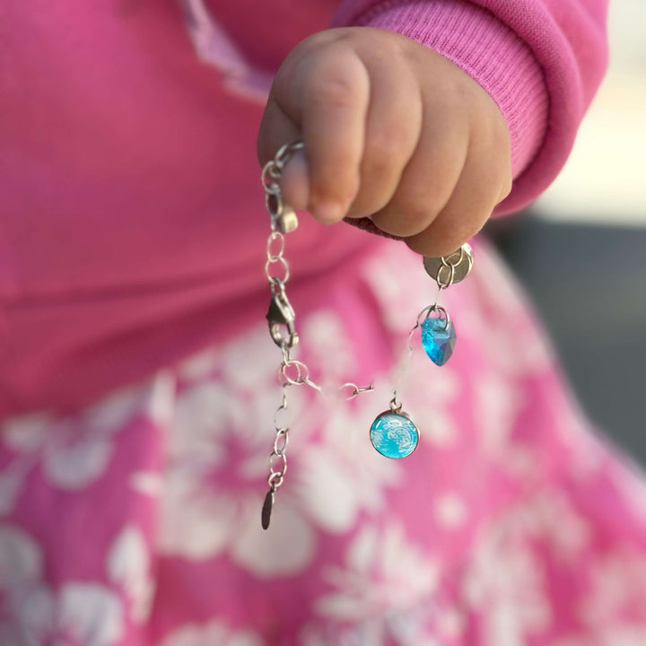 Baby wearing pink holding silver bracelet with blue sonogram pendants and blue birthstone crystals