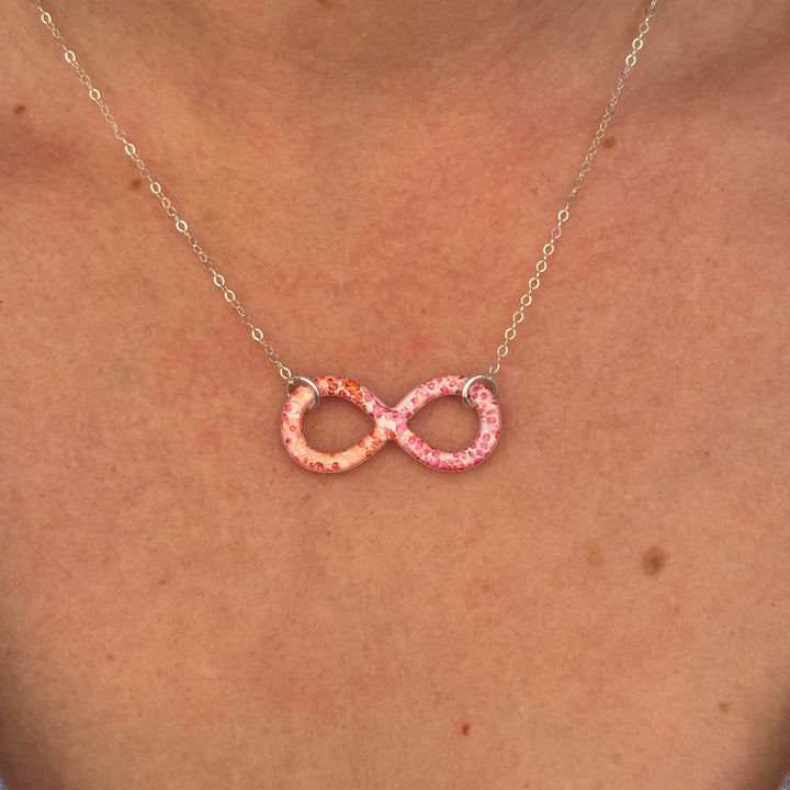 close up of model wearing infinity pendant with orange leukemia cell image in resin on sterling silver adjustable chain
