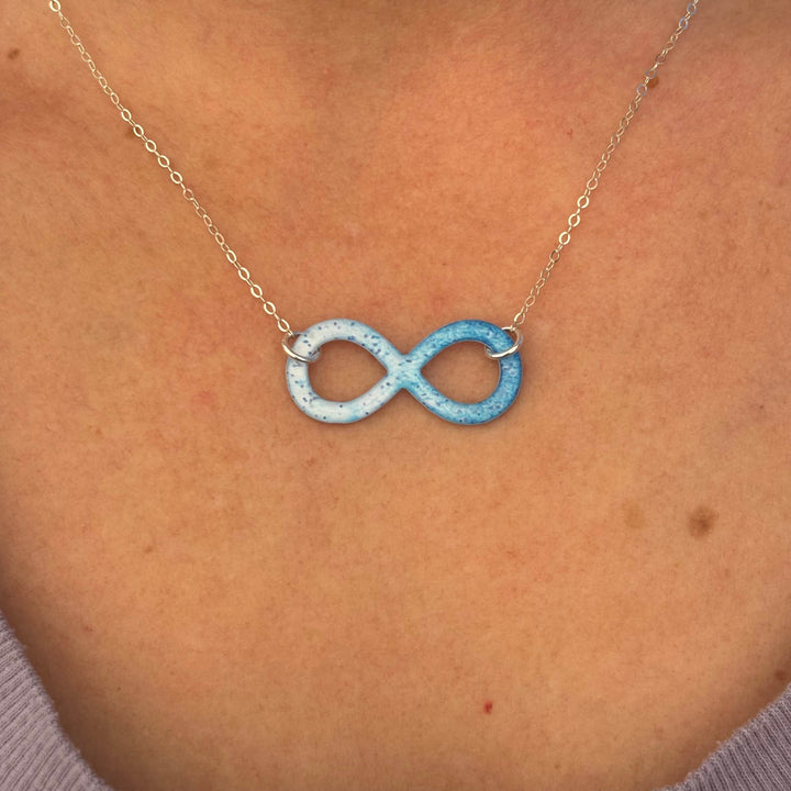 close up of model wearing infinity pendant necklace with multiple sclerosis cell image in resin on sterling silver adjustable chain 
