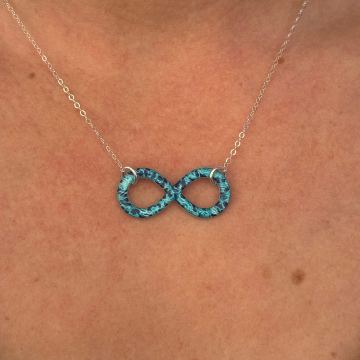 close up of model wearing infinity pendant necklace with ovarian cancer cell image in resin on sterling silver adjustable chain 
