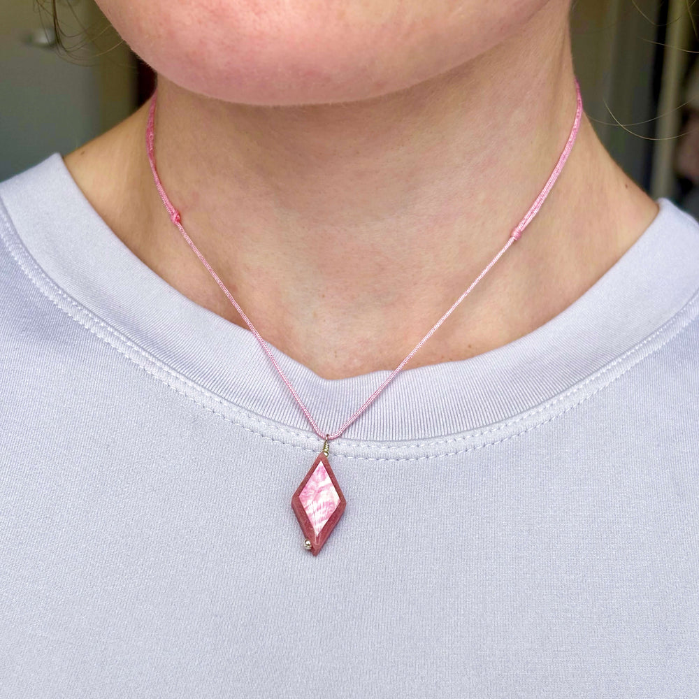 model wearing diamond shaped pink rhodonite stone pendant necklace on pink cord featuring breast cancer cell image in resin