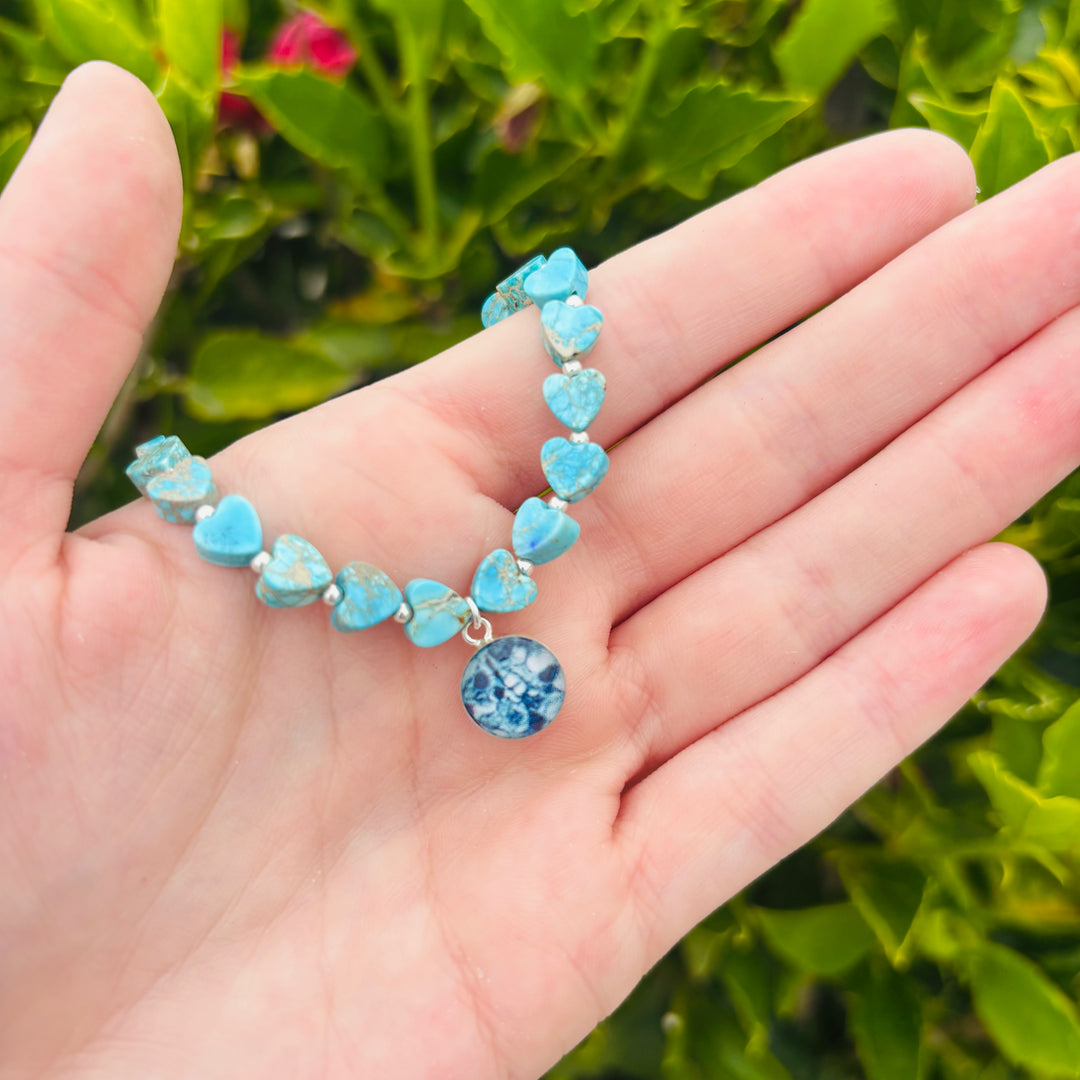 model holding blue sea sediment jasper heart shaped bead bracelet with silver accent beads and round ovarian cancer cell image in resin pendant