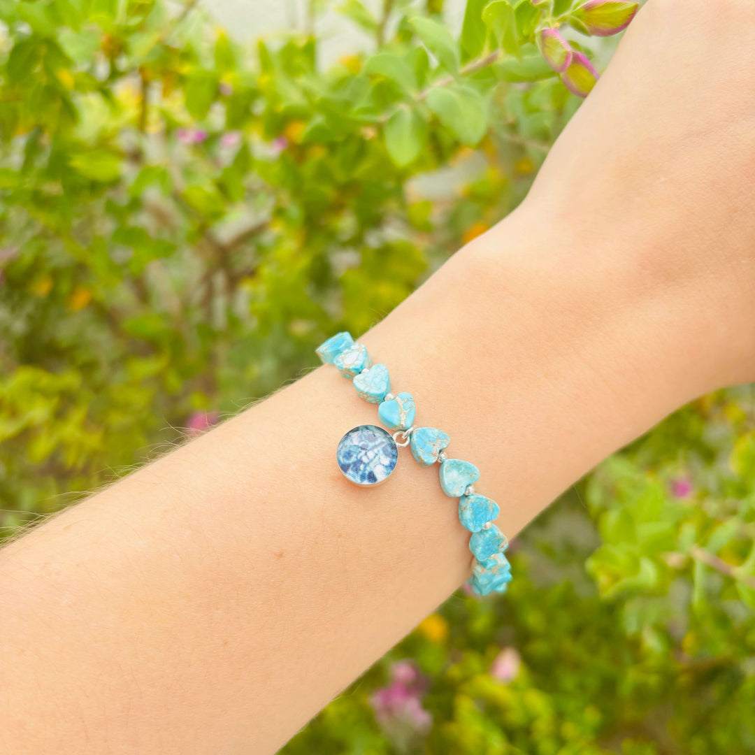 model wearing blue sea sediment jasper heart shaped bead bracelet with silver accent beads and round ovarian cancer cell image in resin pendant