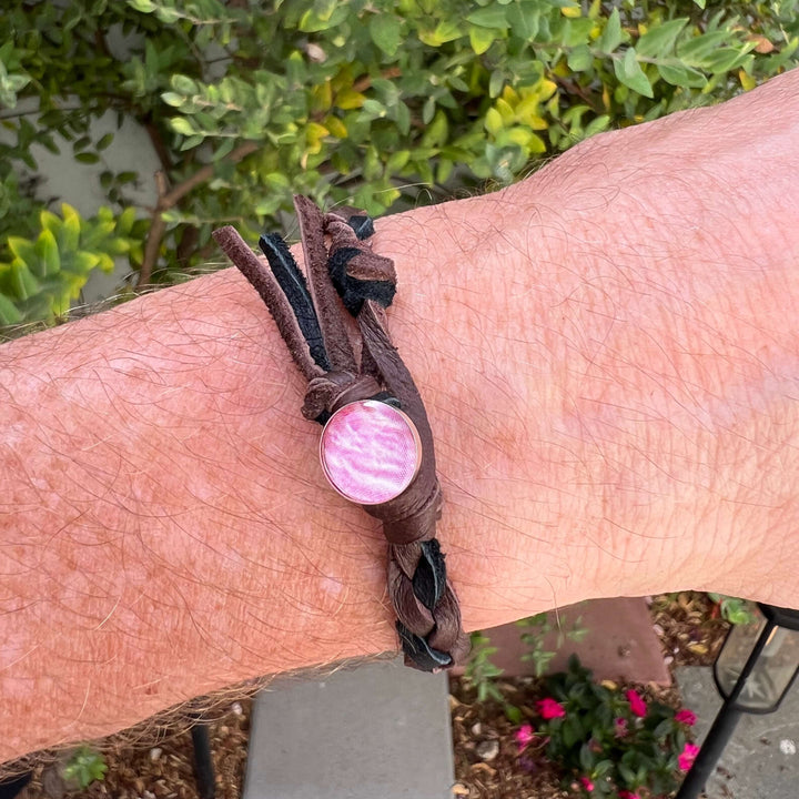 close up of man wearing brown and black guys leather bracelet with round breast cancer cell image in resin pendant