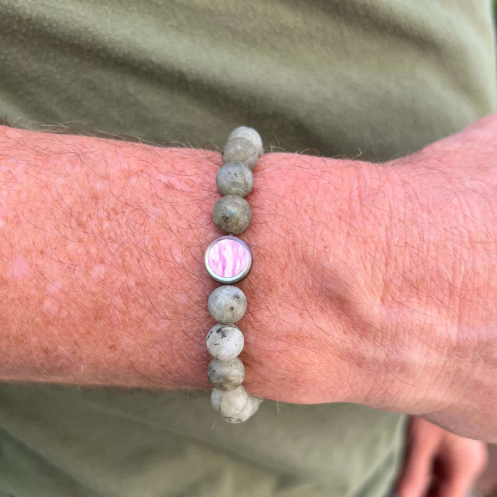 close up of model wearing mens breast cancer bracelet with matte labradorite stones on stretch cord and cell image in resin pendant