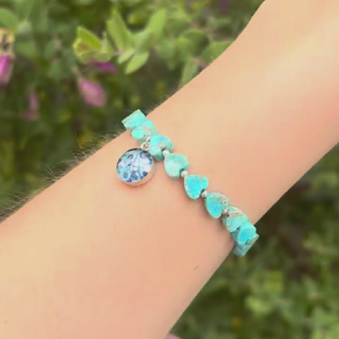 video of model wearing blue sea sediment jasper heart shaped bead bracelet with silver accent beads and round ovarian cancer cell image in resin pendant