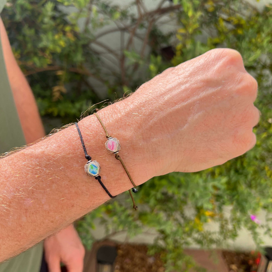 model wearing mens Sterling silver breast cancer cell image in resin pendant on brown adjustable cord and diabetes cell image pendant on black cord bracelet