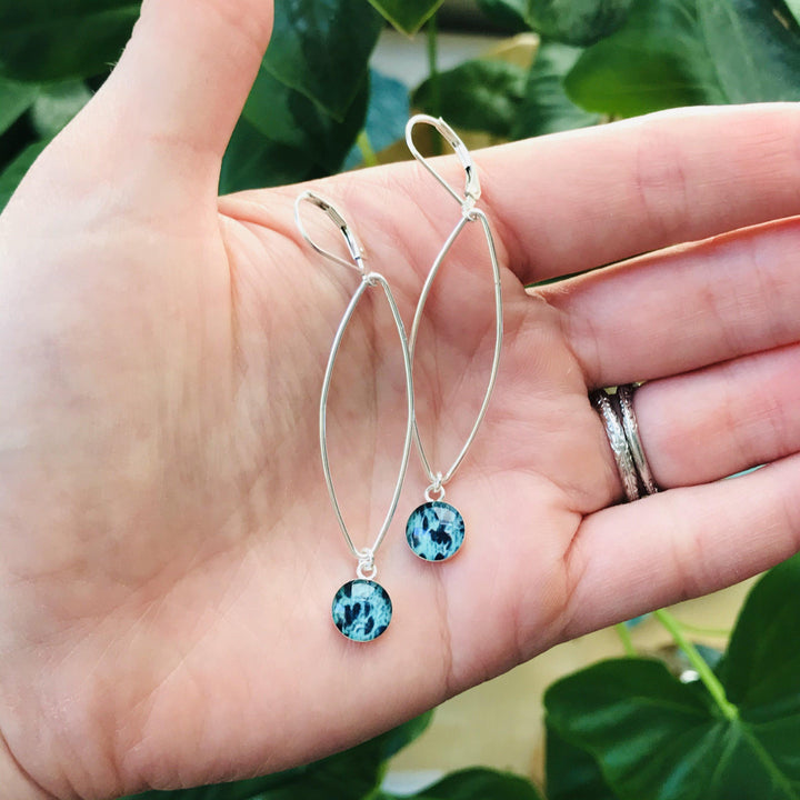 Petal Ovarian Cancer earrings in sterling silver with teal pendants in hand for size.