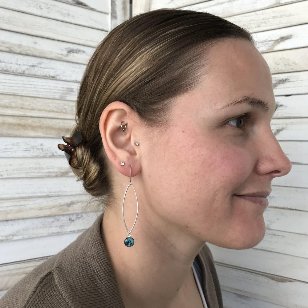 Model wearing Petal Ovarian Cancer earrings in sterling silver with teal hanging pendant. 