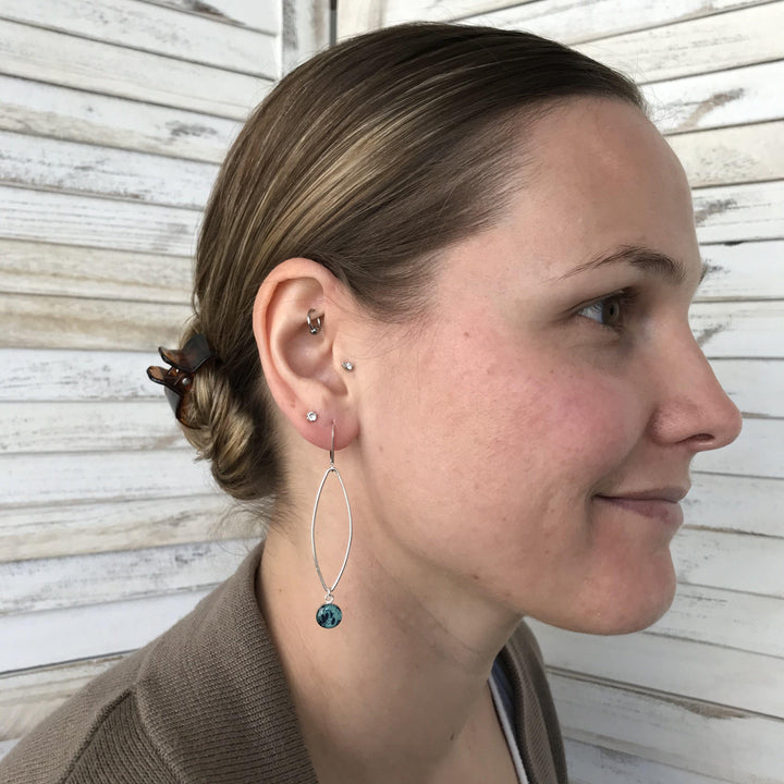 Model wearing Petal Ovarian Cancer earrings in sterling silver with teal hanging pendant. 